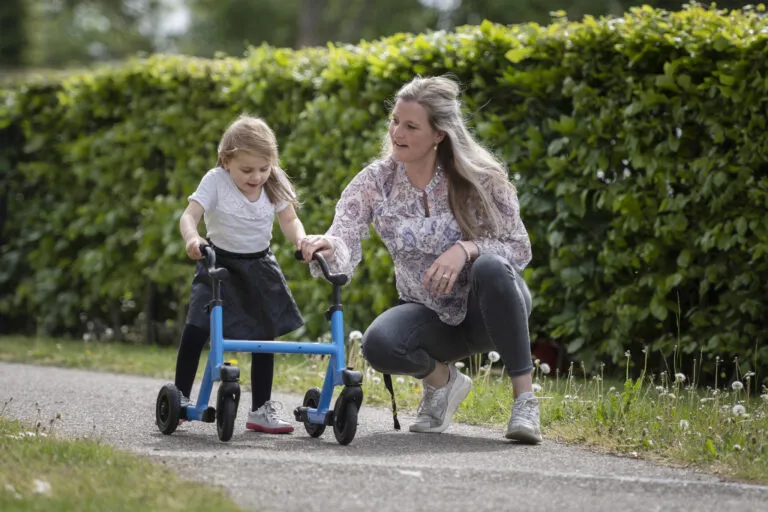 Doelgroep jeugd, kind/cliënt loopt met rollator buiten en begeleider ondersteunt haar hierbij